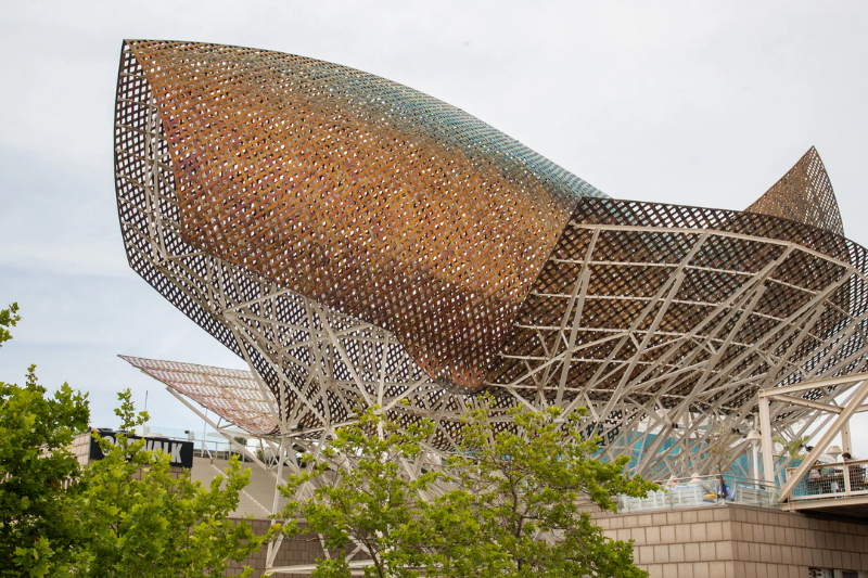 مجسم السمكة الذهبية الشهير في الميناء الأولمبي ببرشلونة مع فنادق حديثة في الخلفية.