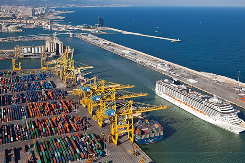 لقطة جوية لميناء برشلونة تظهر الرافعات وسفينة سياحية ومنطقة الحاويات اللوجستية.