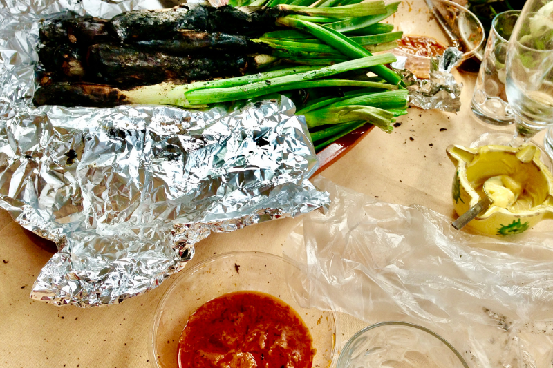 كالسوتس مشوي ملفوف بورق الألمنيوم للحفاظ على حرارته، بجانبه وعاء يحتوي على صلصة الروميسكو (Romesco) التقليدية.