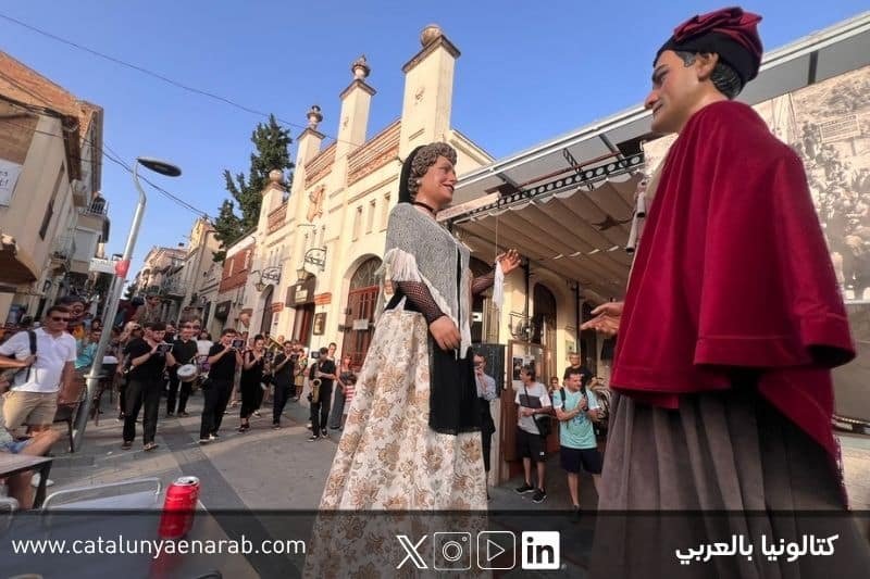شخصيتان عملاقتان تقليديتان تسيران في موكب شعبي في كتالونيا وسط فرقة موسيقية وجمهور